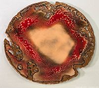 Top-down image of round copper plate with red enamel and natural copper center and edges with holes