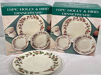 Two boxed sets of 16-piece Holly and Bird dinnerware with festive holly and bird design, shown with one plate outside the box.