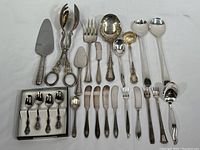 Full view of all silverplate serving ware items arranged on a white cloth surface showing variety and quantity.