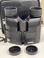 Black Nikon 7x20CF Porro prism binoculars with adjustable eyecups and lens caps placed in front, showing front view with Nikon logo visible.