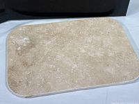 Close-up photo of the travertine cheese board showing beige textured natural stone surface with rounded corners.