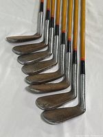 Photo showing all eight golf clubs lined up with wood shafts and metal heads, showing wear and tarnishing on heads.
