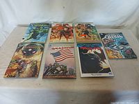 Top-down photo showing all 7 graphic novels laid flat on a surface in two rows. Covers visible showing various DC and Marvel titles including Green Lantern and Captain America.