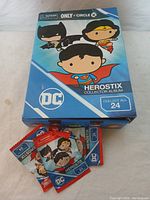 Closed collector album/box with DC Herostix cover art and three sealed booster packs.