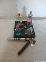 Collection of small collectible bottles on a black tray; includes various shaped and colored bottles plus two cigar-shaped items on the side.