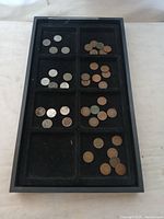 Black divided tray holding an assortment of coins including steel and wheat pennies, showing variety of conditions and colors.