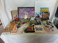 Wide view of assorted items including books, toys, playing cards, and novelty items arranged on table.