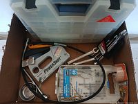 View of the full lot inside a cardboard box showing PowerShot staple gun, wrenches, Allen wrenches, drill bits, and other components.