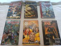 Top-down view of six graphic novels arranged in two rows of three showing colorful comic covers with superheroes.