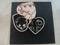 Top view of two heart-shaped jewelry boxes, one open showing charm bracelet and the other open showing loose beads and charms.