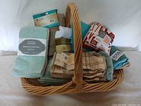 Full view of wicker basket filled with assorted new kitchen hand towels, some in original packaging