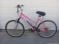 Front angled view of pink Diamondback bike showing overall condition including tires, saddle, frame and handlebars in front of a garage door.