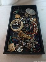 Overview of mixed crafting jewelry in black tray including bracelets, earrings, necklaces, and pendants