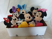 Box containing assorted Mickey and Minnie Mouse plush toys arranged with faces visible.