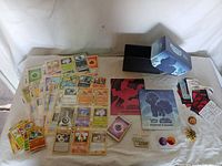Wide photo of all lot items including the Pokémon cards, storage box, player’s guides, sleeves, and tokens.