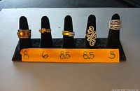 Set of 5 gold-tone rings in sizes 8, 6, 8.5, 8.5, and 5 shown on black ring holders with size labeled in front
