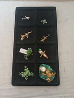 Eight small animal brooches displayed on black tray with divided sections