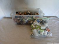 Photo showing plastic container filled approximately half full with various wooden and plastic spools containing sewing thread in multiple colors.
