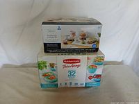 Photo of two boxed sets of food storage containers: a large Rubbermaid Take Alongs 32-piece set and a smaller Mainstays 9-piece set. Both are food storage containers with clear plastic bodies and lids; Rubbermaid box is sealed, Mainstays box is opened but containers appear unused.