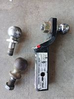 Trailer hitch with two attached chrome hitch balls and one separate chrome hitch ball on concrete floor.
