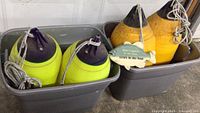 Two pairs of yellow buoys with black tops inside gray plastic bins.