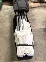 Collapsible metal frame folded and wrapped with white fabric canopy top in black carry bag on floor.