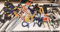 A wide variety of clamps arranged on a table showing different sizes and types including bar clamps, hand clamps, and spring clamps.