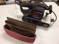 Full view of the Craftsman belt sander with extra sanding belts laid in front, showing four belts are unused.