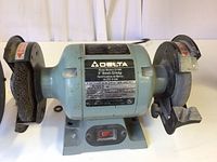 Front view of Delta 6 inch bench grinder showing grinding and wire brush wheels, power switch, and labels.