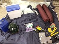 Photo showing the blue Coleman fuel container, green Coleman propane lantern, small ice chest, and some smaller items including rope, whistle, stakes, and cookware.