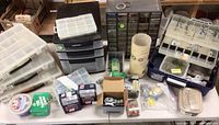 Wide view of the entire hardware lot laid out on a table including multiple plastic organizers, boxes, and containers holding screws, fasteners, washers, and hooks.