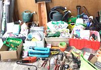 Overall view of dozens of garden items on concrete floor against pegboard, showing variety of hoses, fertilizers, tools and containers