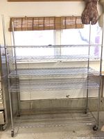 Front view of large metal rolling steel shelf with five wire mesh shelves in light industrial setting.
