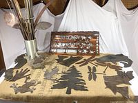 Metal and copper cut out art pieces displayed on burlap and a white backdrop, including animal and nature shapes with a decorative American flag