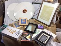 Two mini tabletop easels in box, blank frames, round canvases, and small painting accessories shown on a fabric backdrop.