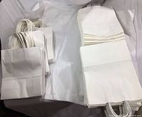 Overview showing stacks of both sizes of plain white gift bags with twisted handles.
