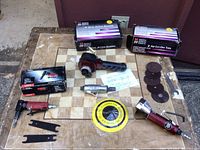 Overview of pneumatic tools including the angle die grinder, dual action sander, air cut off tool, sanding discs and spanner wrenches arranged on a board.