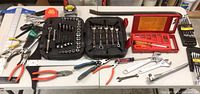 Wide view showing most tools including socket sets in black cases, various wrenches, pliers, tape measures and screwdrivers laid out on table.
