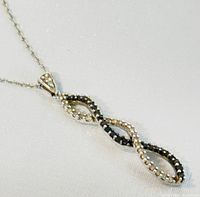 Close-up photo of the pendant showing the infinity twist design with alternating black and white diamonds set in 10K white gold.