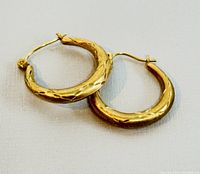 Pair of small 10K yellow gold hoop earrings laid flat on a surface showing textured pattern and hinge clasp.