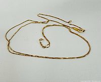 Full length laid out image of the thin yellow gold necklace chain showing the clasp and chain design.