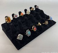 Full display of all twelve vintage signed rings on black velvet ring display rack, showing variety of stones and styles.