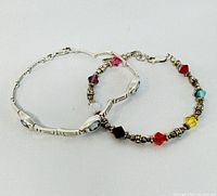 Two 7.5 inch silver bracelets shown, one with blue gemstones and geometric links, the other beaded with multi-colored crystal beads.