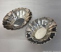 Pair of two small sterling silver bowls with scalloped edges shown from top side on a gray background.