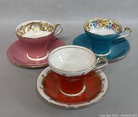 Front view of three Aynsley vintage teacups with matching saucers showing their unique colors and gold detailing.