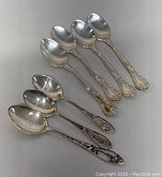 Seven sterling silver teaspoons arranged in two groups, showing the four Birks teaspoons with floral handles and three additional stamped sterling teaspoons with varied designs.