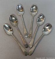 Top view of six sterling silver teaspoons arranged in a fan shape showing floral pattern on handles and polished bowls.