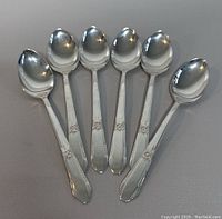 Photo of six Northumbria sterling silver teaspoons arranged side by side showing the front side with decorative floral pattern on handles.