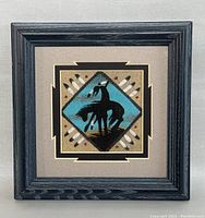 Full view of framed sandpainting with black wood frame and beige matting, featuring Native American figure on horseback.