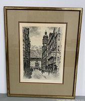 Full front view of framed etching showing building-lined street in Innsbruck, Austria with a mountainous backdrop.